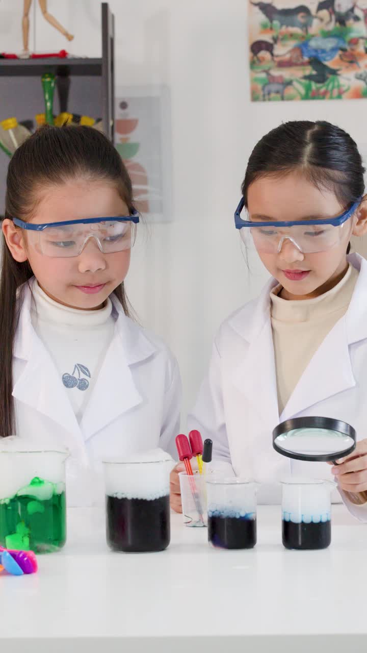 Dua gadis muda Asia mengenakan jas lab melakukan eksperimen sains dan merayakannya dengan tos.