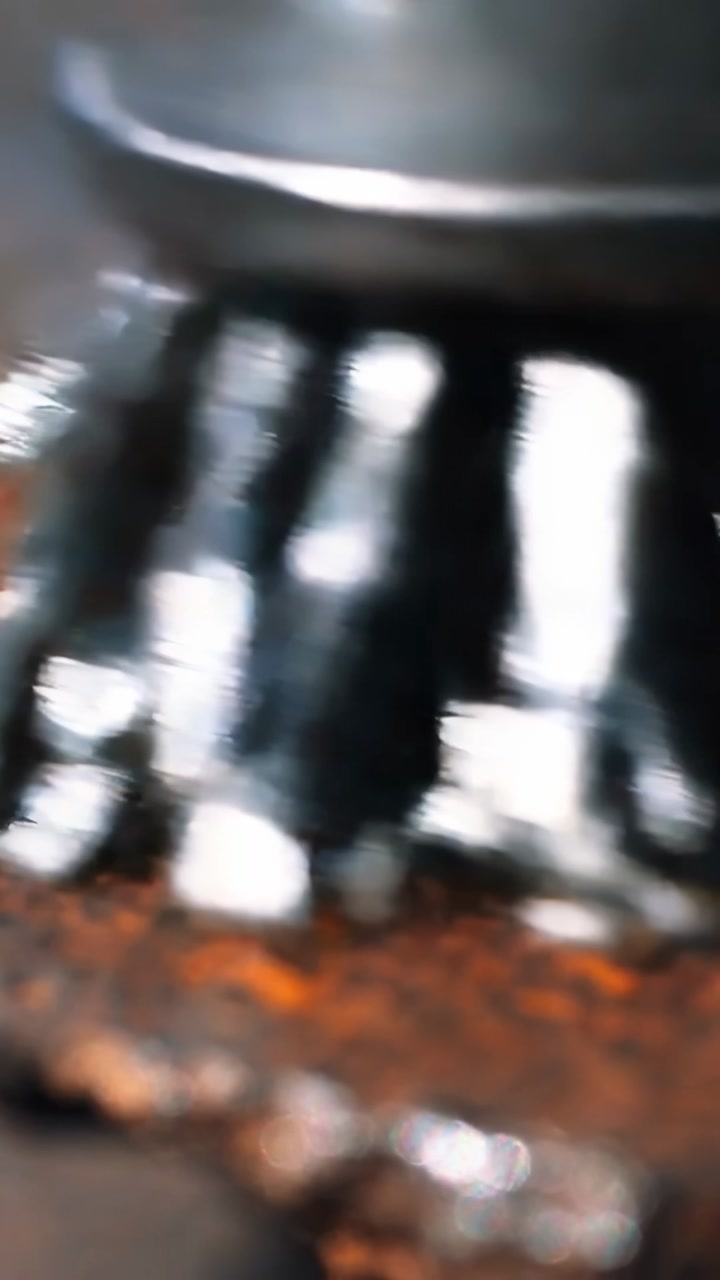 Vertical video: Lowering metal rotary brush head making contact at workbench, removing rust