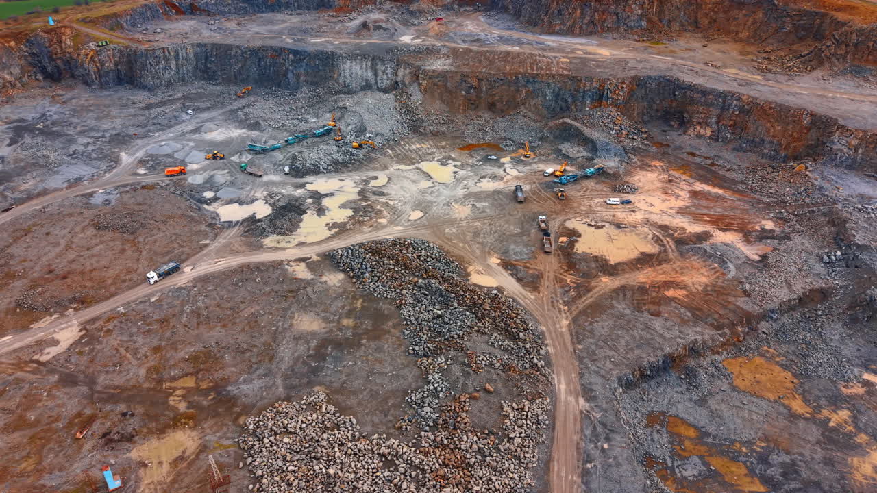 High angle view of active mining site with vehicles. Aerial perspective of an open pit quarry showing multiple work zones, piles of rock, and trucks