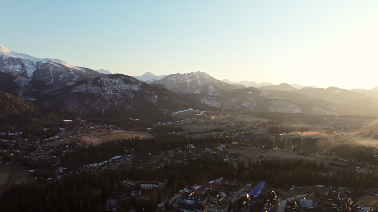 Pan drone shot of Tatra Mountains with snow and Zakopane cityscape at sunrise in Podhale region, Poland