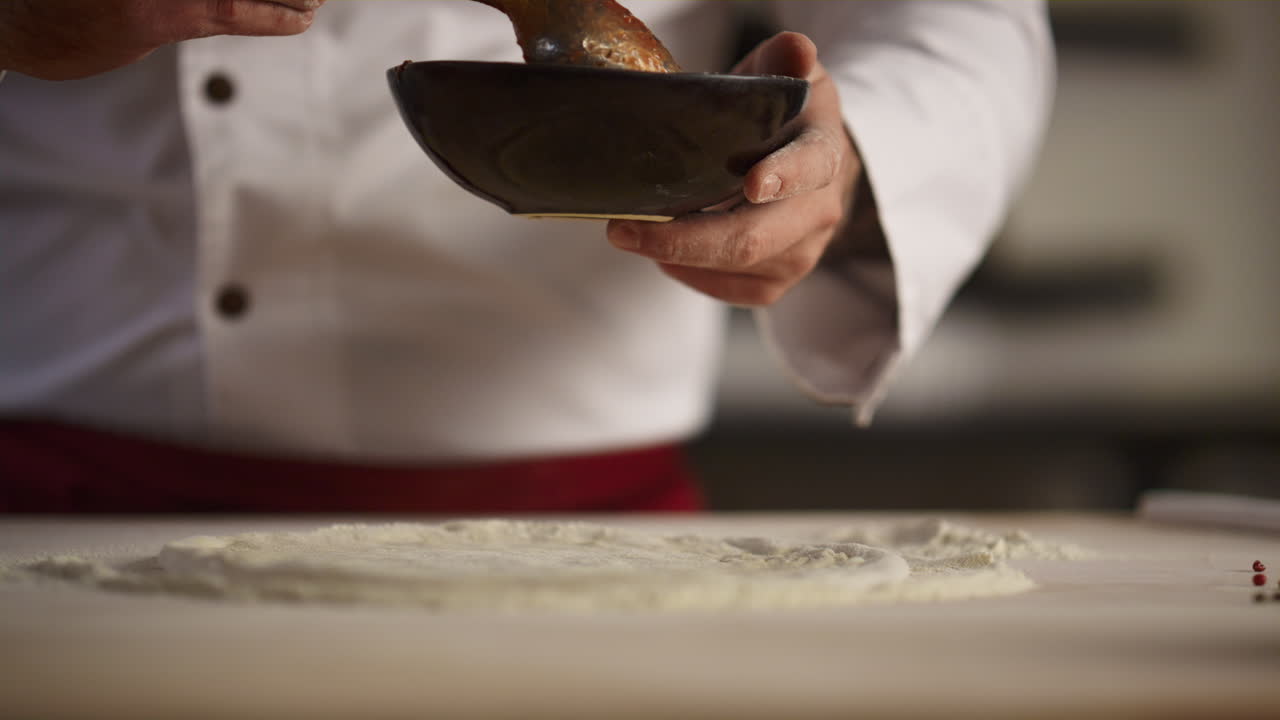 Chef che cucina pizza italiana su tagliere di legno. Mani d'uomo che stendono la salsa di pomodoro.