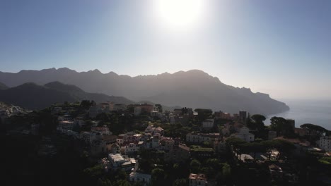 Drone-flying-over-a-mountain-ridge-revealing-a-village-on-the-Amalfi-coastline-in-the-early-morning-in-Italy-in-4k