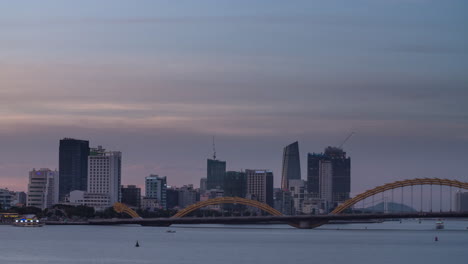 lapso de tiempo de la ciudad del horizonte urbano moderno - una transición de día a noche con luces de neón, puente de dragón y barcos en el río en vietnam asia