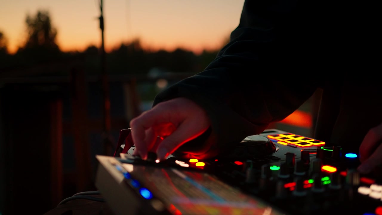 DJ justerer lydmixer ved udendørs arrangement i solnedgang