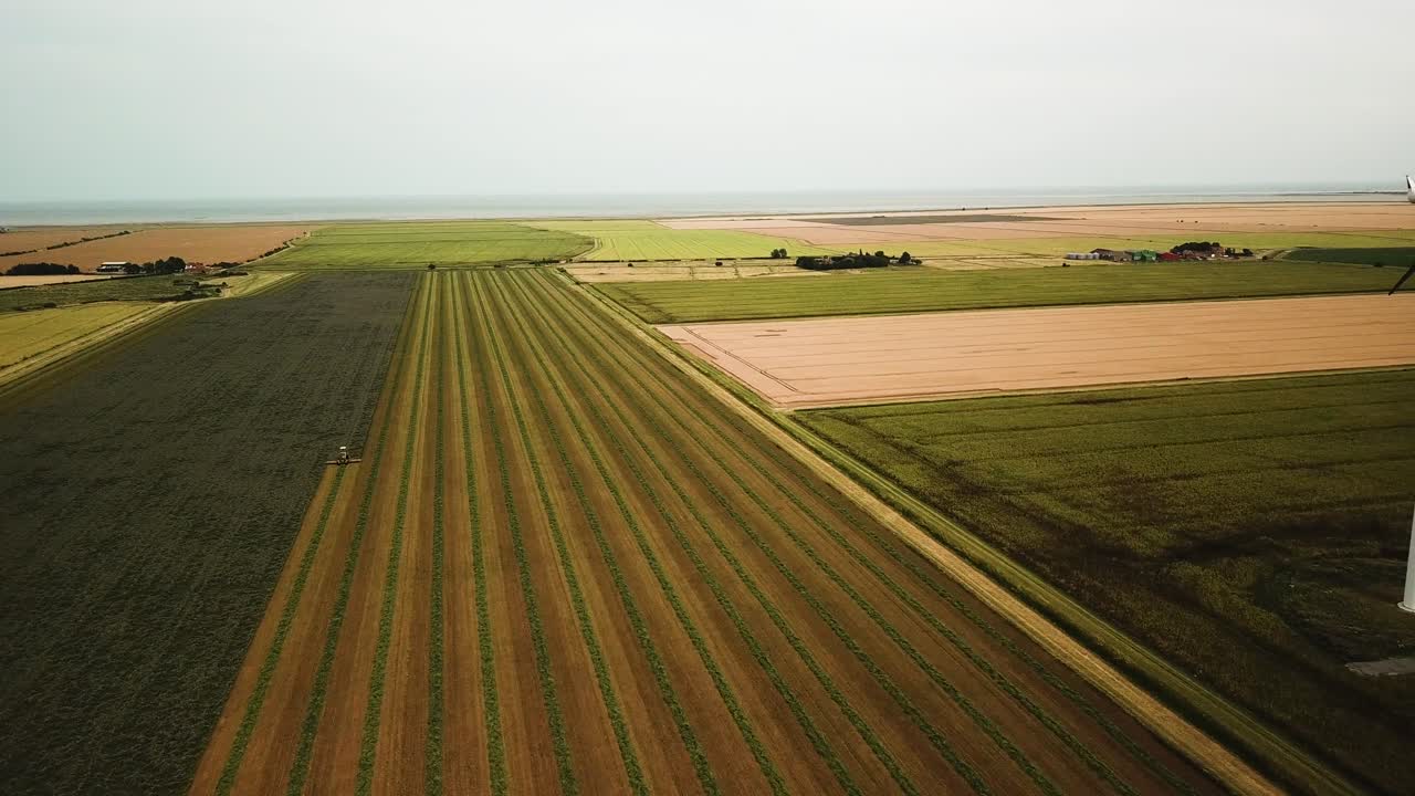 Wide drone shot of a tractor cutting rows of hay