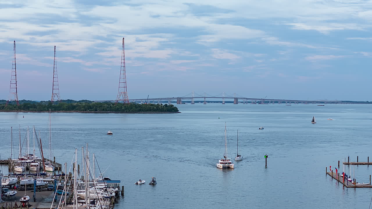 Maryland, ABD'deki Chesapeake Koyu'nda, marina yakınında gün batımında yelken açan yelkenliler. Uzakta Chesapeake Bay Köprüsü. timelapse, geniş çekim.