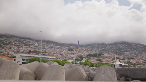 Hillside-cityscape-of-Funchal,-Madeira-with-overcast-skies-and-concrete-sea-defences