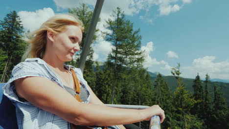 an active woman enjoys a ride on a cable car over a forest surrounded by mountains 4k video