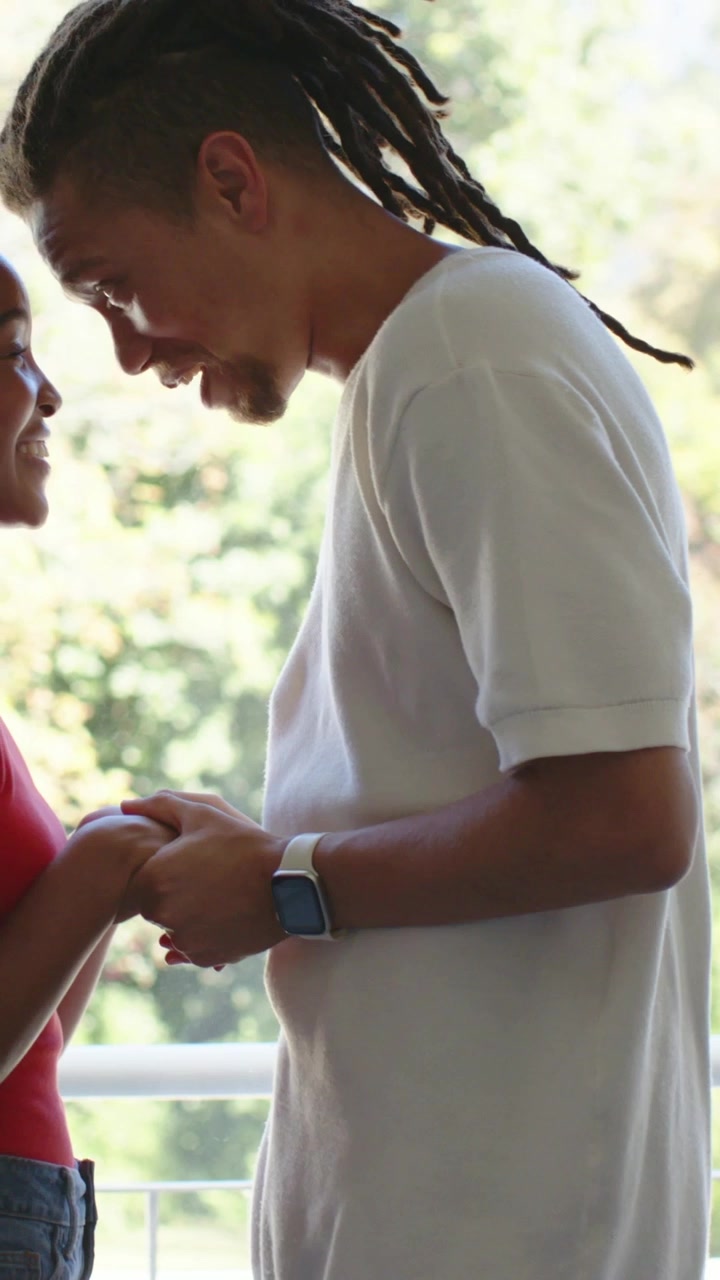Video vertical: Hombre abrazando, devolviendo el abrazo mientras la mujer lo rodea con los brazos en el balcón, reloj que muestra afecto.