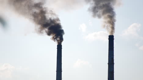 dark silhouettes of factory pipes producing dark smoke into the sky. air pollution from industry. light blue sky backdrop.