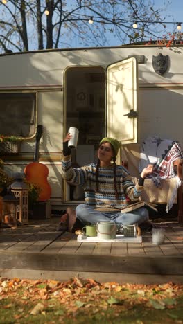 woman relaxing outdoors with a book and coffee by an rv in autumn