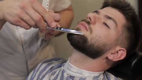 Client-with-black-beard-during-beard-shaving-in-barber-shop.-Groom,-masculine