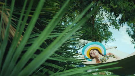 away from civilization, a young woman relaxes on a hammock. around the green palm trees, the blue sky