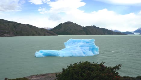 iceberg en agua de lago glacial con picos de glaciares y andes en segundo plano