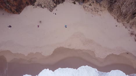 aerial ascending top down view of a cliffside beach at praia da ursa, portugal