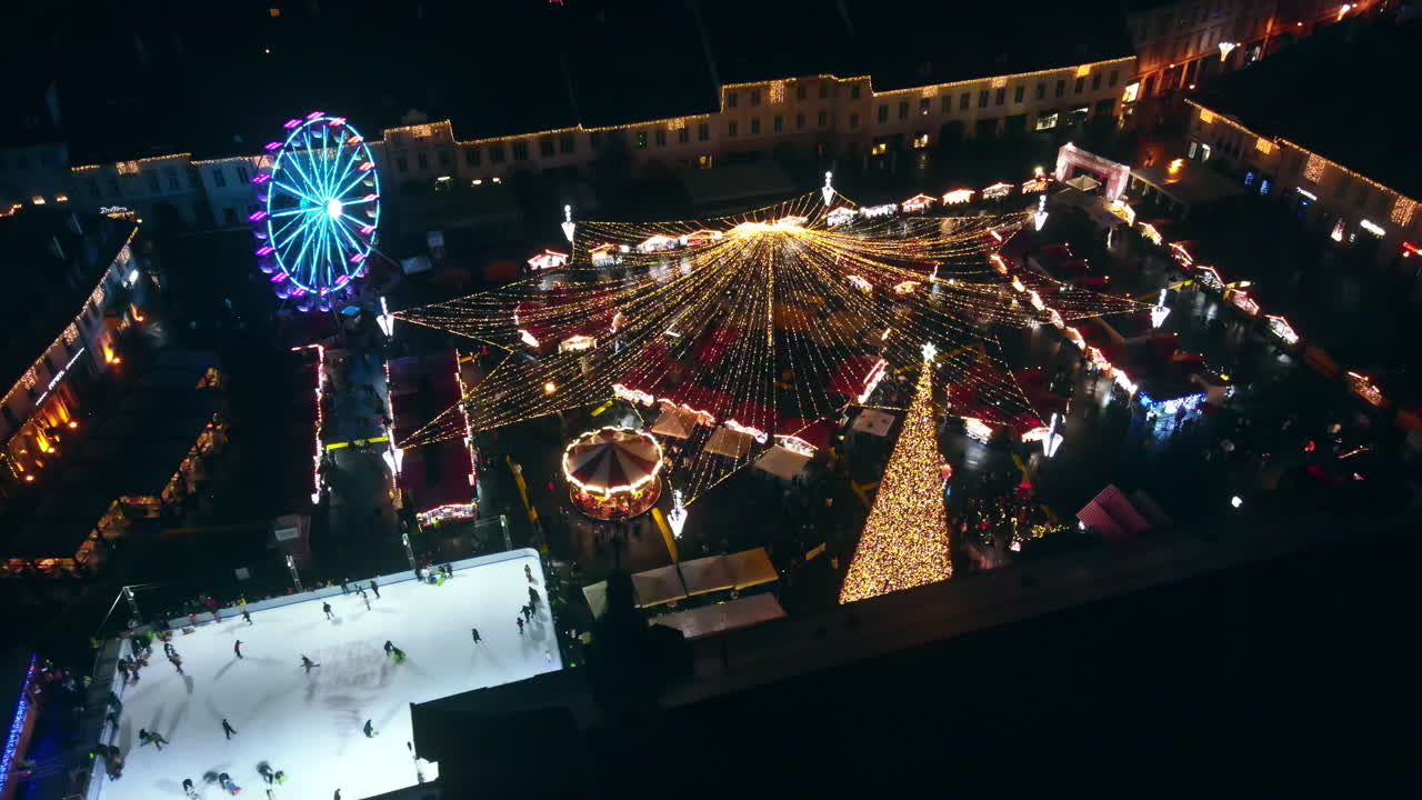 Aerial drone view of The Big Square in Sibiu at night, Romania. Old city centre decorated for Christmas. Ferris wheel, skating rink, people