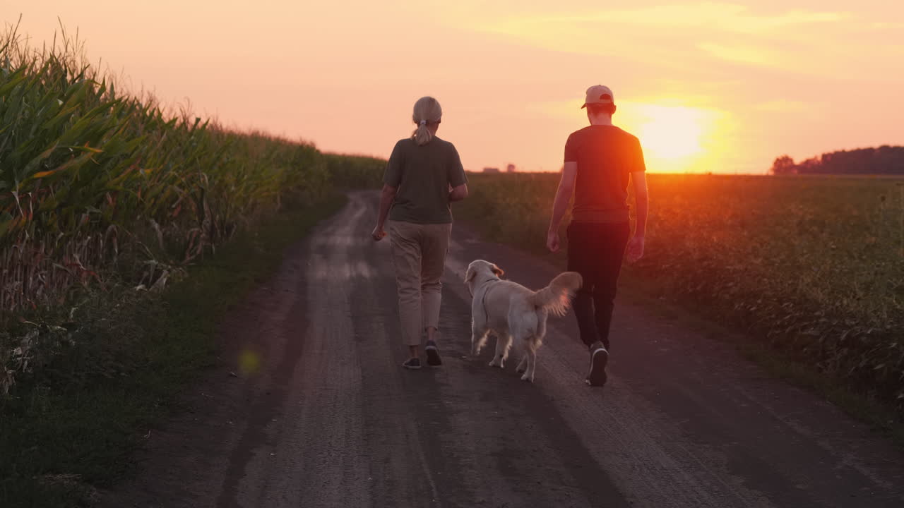 una pareja paseando con un perro en un camino de campo al atardecer