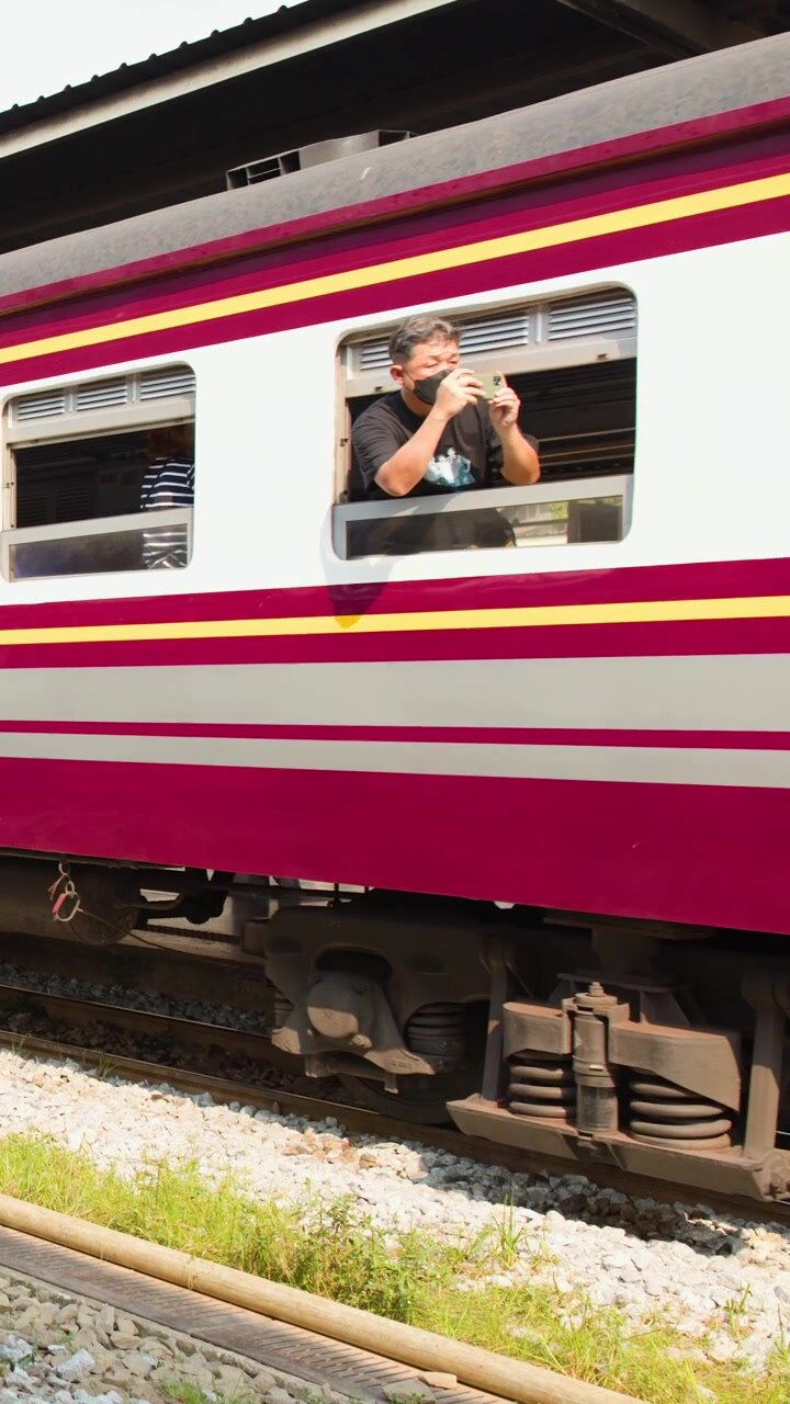 A side view tracking shot of colorful passenger train carriages moving along tracks in Bangkok