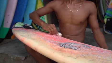 joven encerado de tablas de surf en la tienda de surf, lombok, indonesia