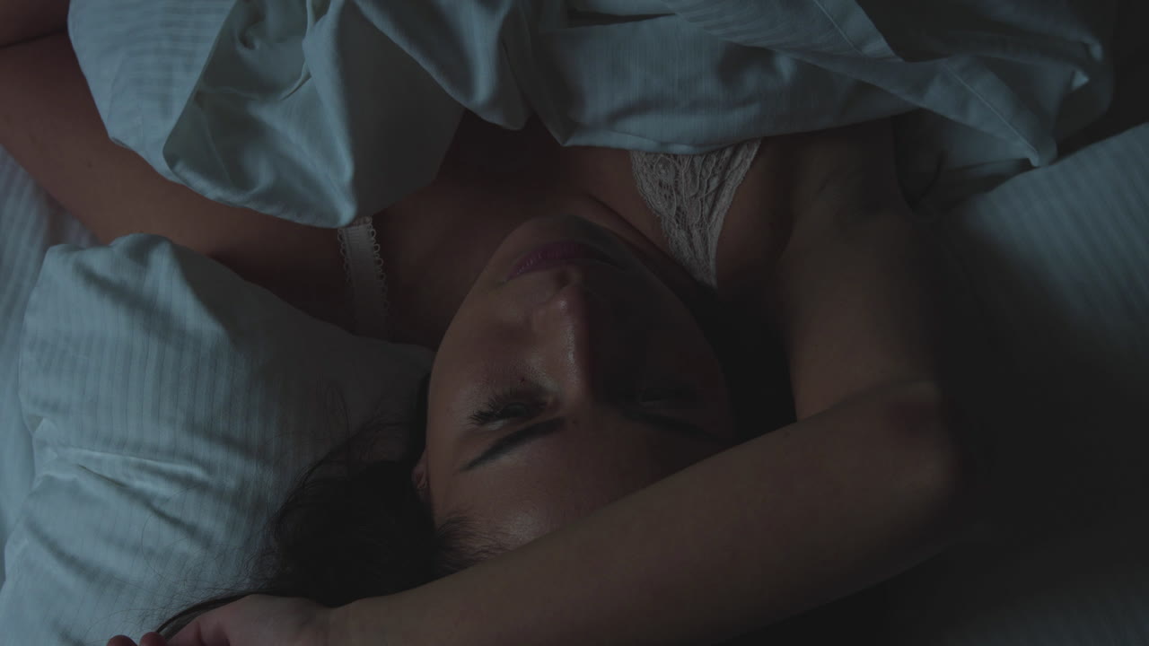 Top view of a young woman lying on a pillow. It's night. The woman is lying in bed and cannot fall asleep. She is restless and nervous. He has nightmares. He suffers from insomnia. Sleepless night