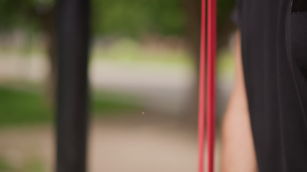 CloseUp Man Forearm And Biceps Holding Red Band, Trainer Rolled Sleeve Reveals Muscle And Tattoo, Textured Skin And Grip Detail Emphasize Strength And Technique, Outdoor Workout Vibe