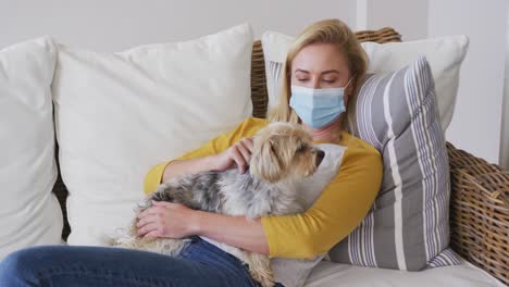 Woman-wearing-face-mask-holding-her-pet-dog-at-home