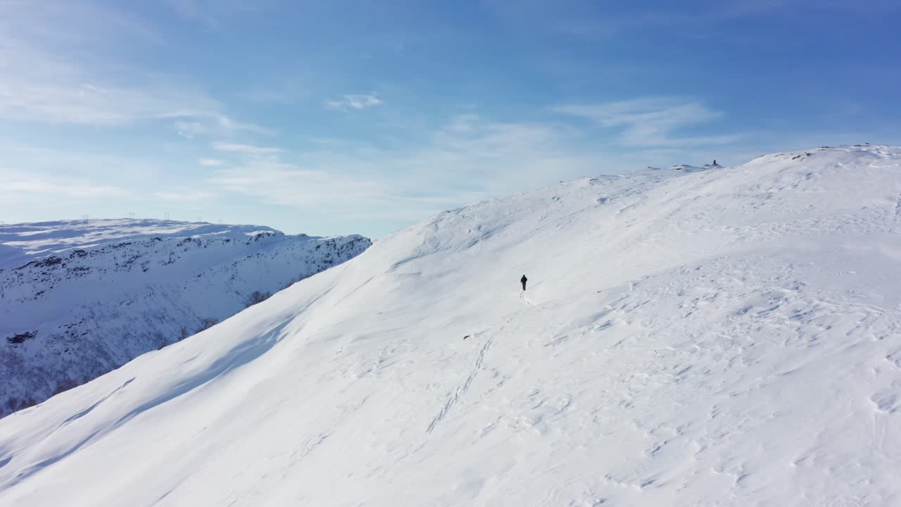Aerial shot slowly overtaking person walking on ski uphill, beautiful snow covered Landscape