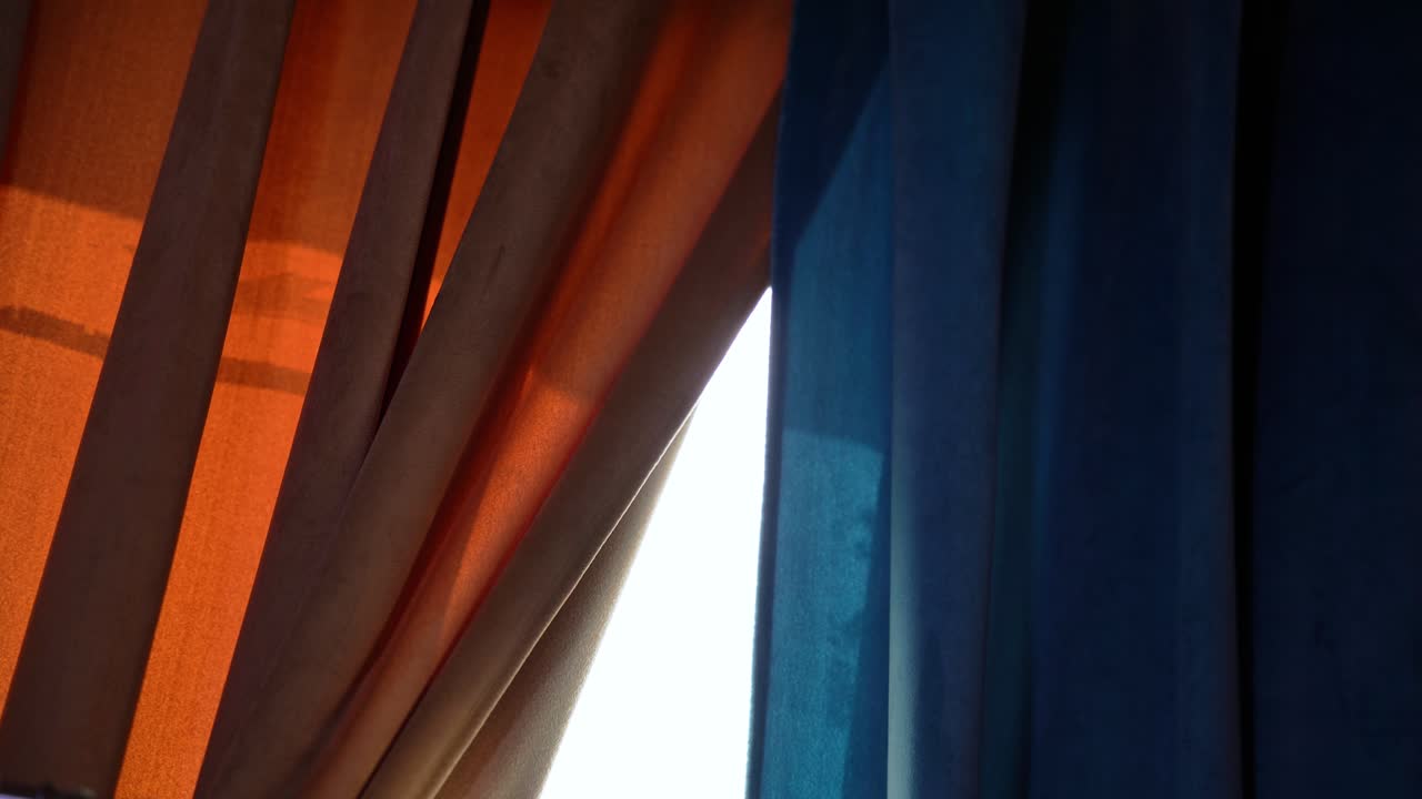 La calda luce del sole filtra attraverso tende di velluto arancioni e blu. Ideale per interni, texture, atmosfera o immagini narrative cinematografiche