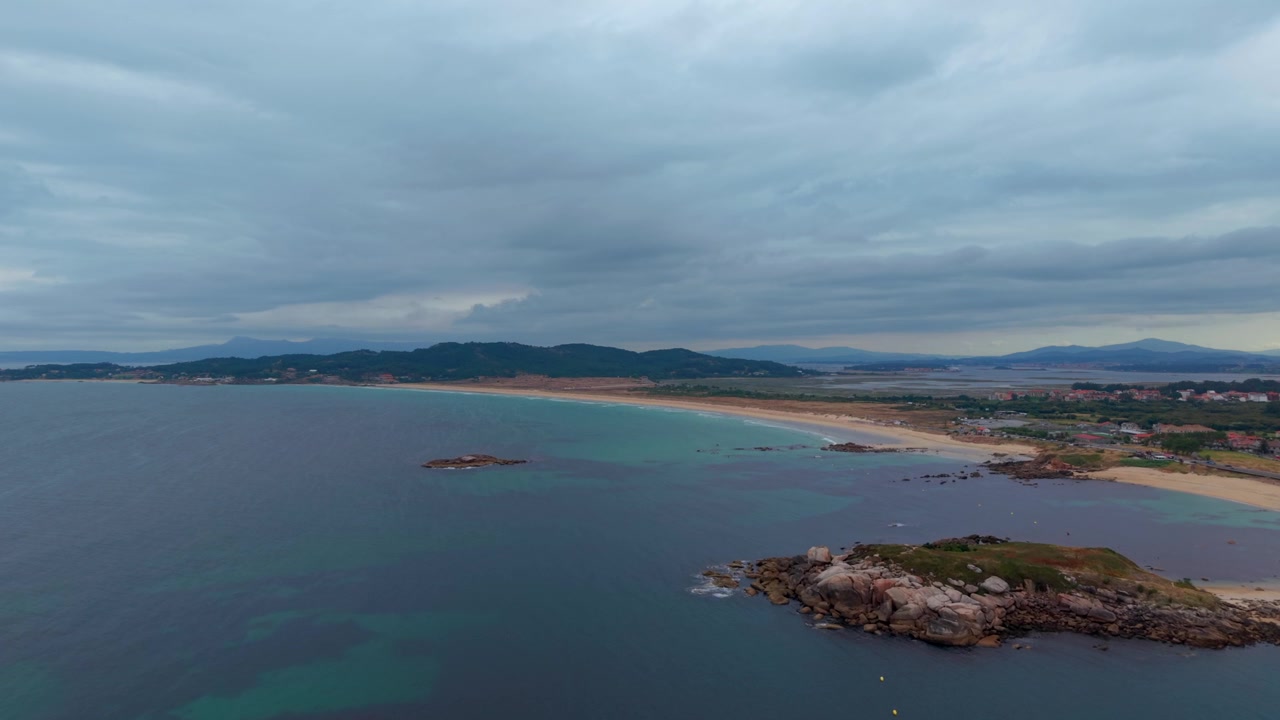 Bred droneudsigt fra luften af den lange A Lanzada strand med en klippeø og roligt hav under en stemningsfuld overskyet himmel i Pontevedra, Galicien, Spanien.