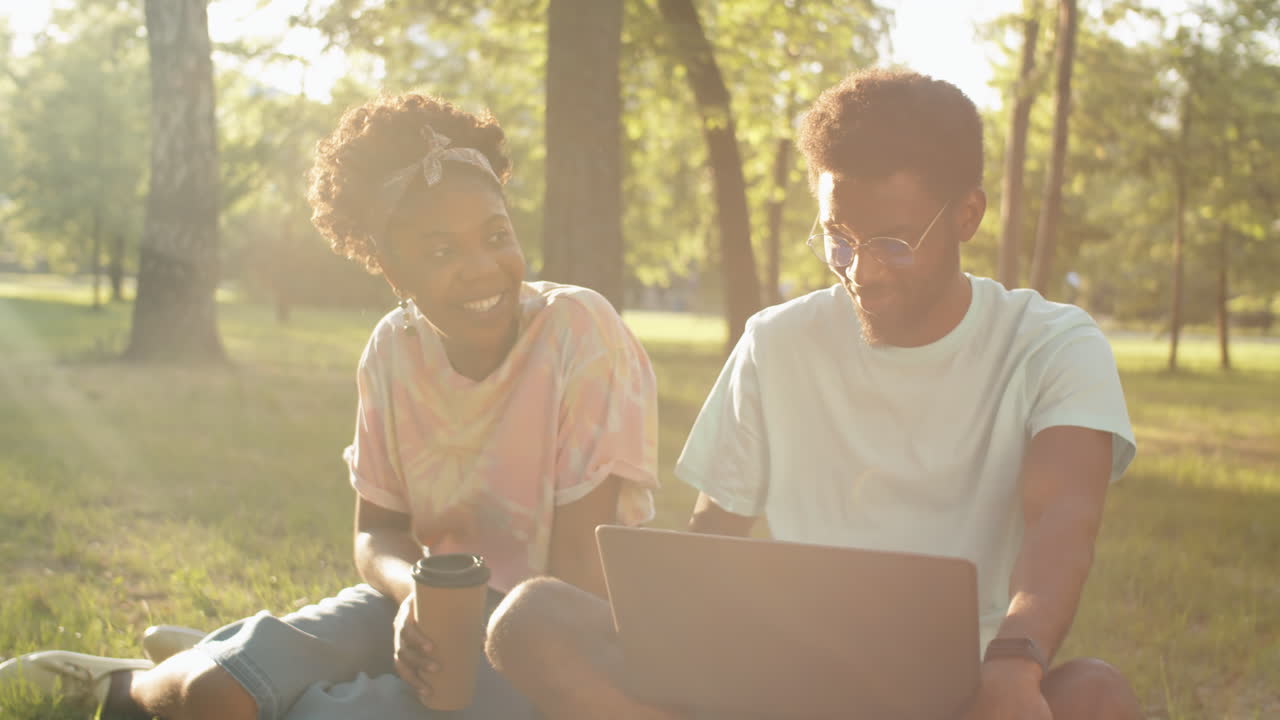 African American Friends Chatting, Having Coffee and Using Laptop in Park