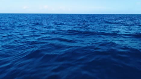 Aerial-dolly-push-in-above-ocean-waves-slowly-building,-deep-blue-water-texture