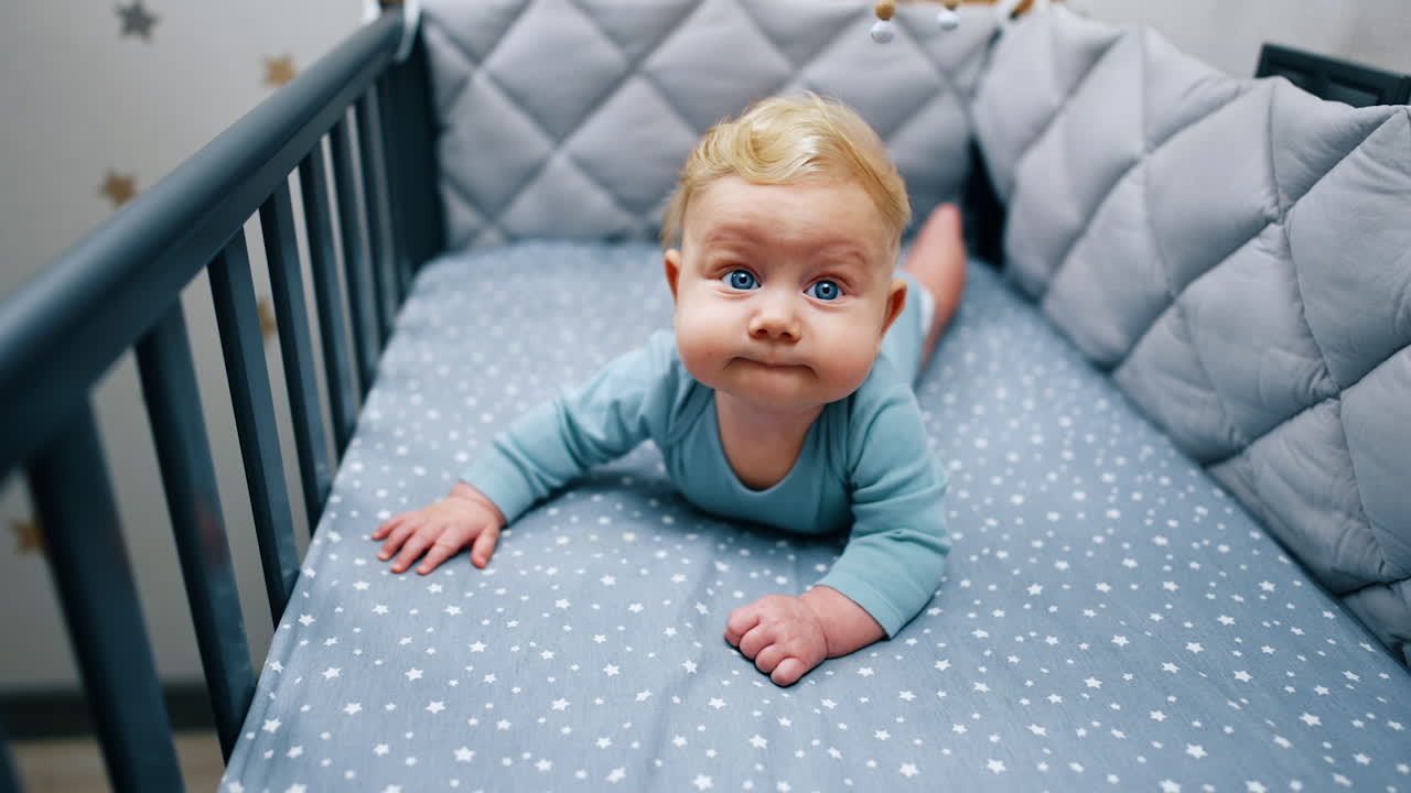 Funny baby boy with adorable plump cheeks lies in his crib. Beautiful blond infant at home.