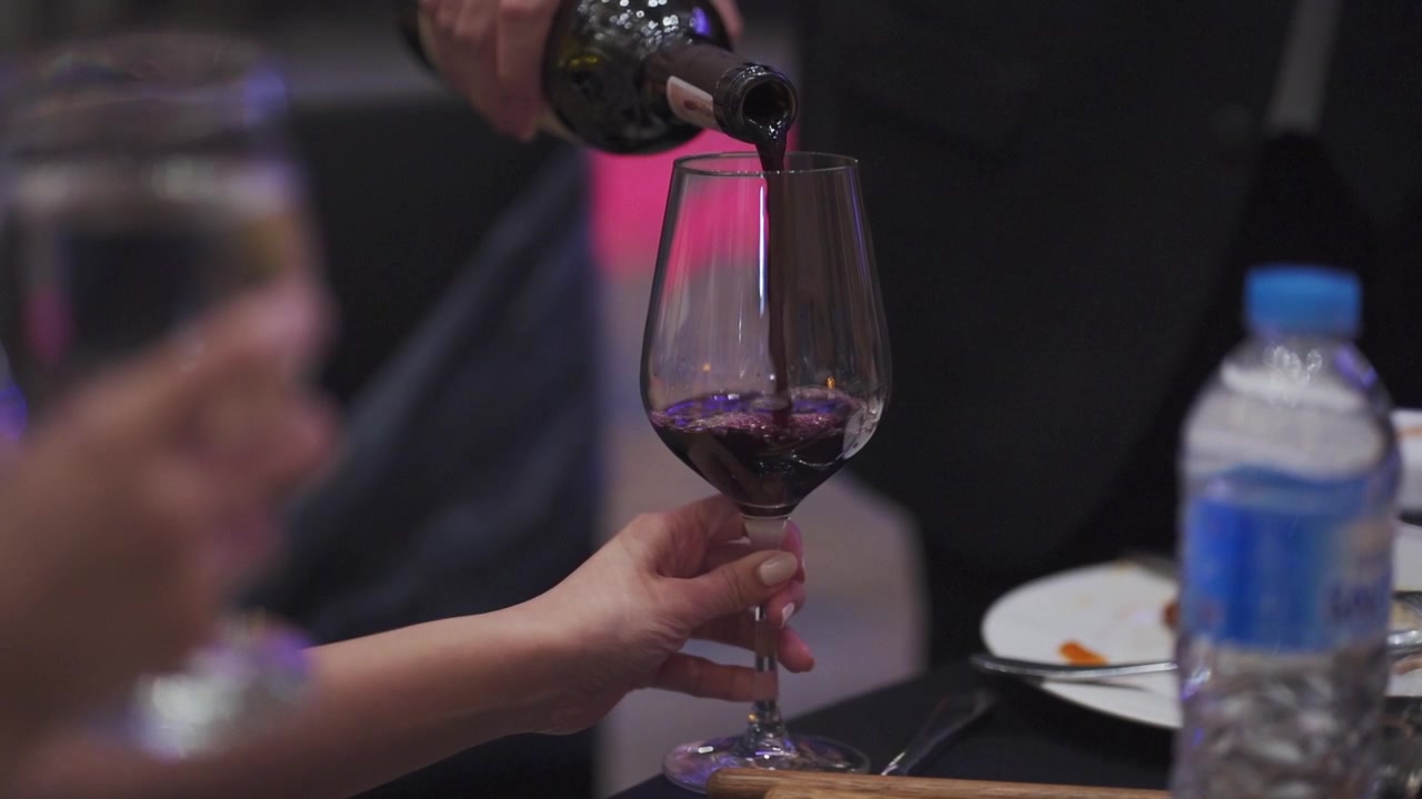 Personas celebrando y levantando copas de vino para un brindis en una cena de noche en interiores.