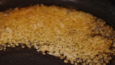 close up shot of pan frying, sauteing and caramelizing miced garlic, boiling in shimmering cooking oil with high heat, aromatic smell and sizzling sound