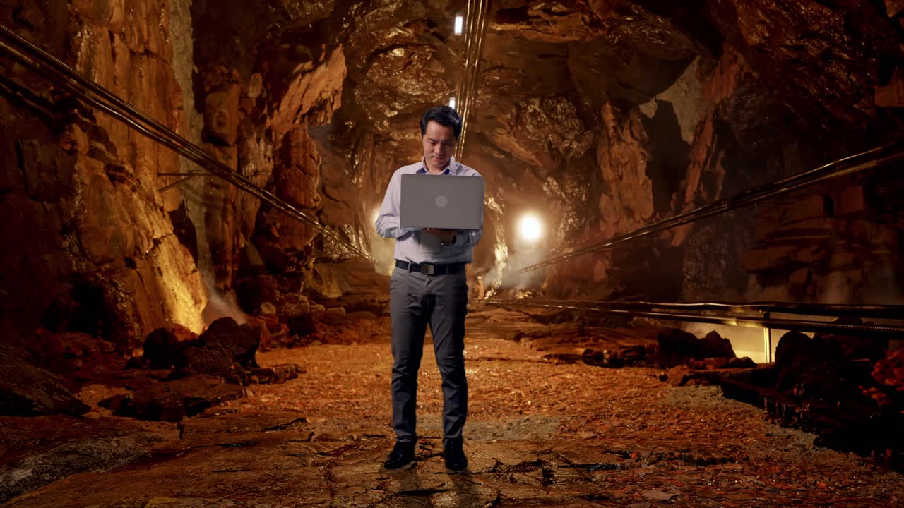 Full Body Of An Asian Male Professional Worker Standing With His Laptop In Underground Mine Tunnel, Working Continuously