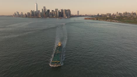 cinematic aerial view of cargo ship sailing on hudson river with new york financial district in background at sunset, united states of america