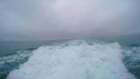 aggressive and large wake waves caused by large dolphin and whale spotting boat in the middle of the large ocean on very cloudy moody day