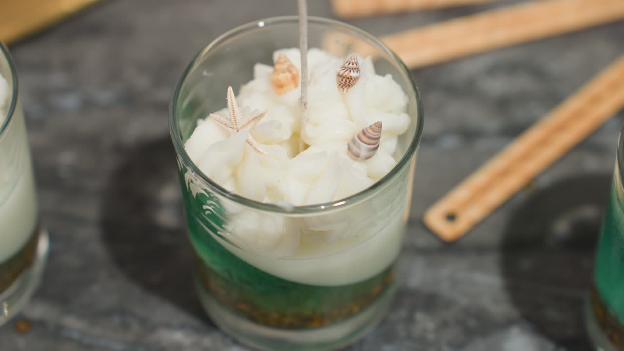 Hand view of chef gently placing shell decoration into creamy ice cream swirl inside layered dessert glass, showing attention to detail and artistic food presentation in culinary design