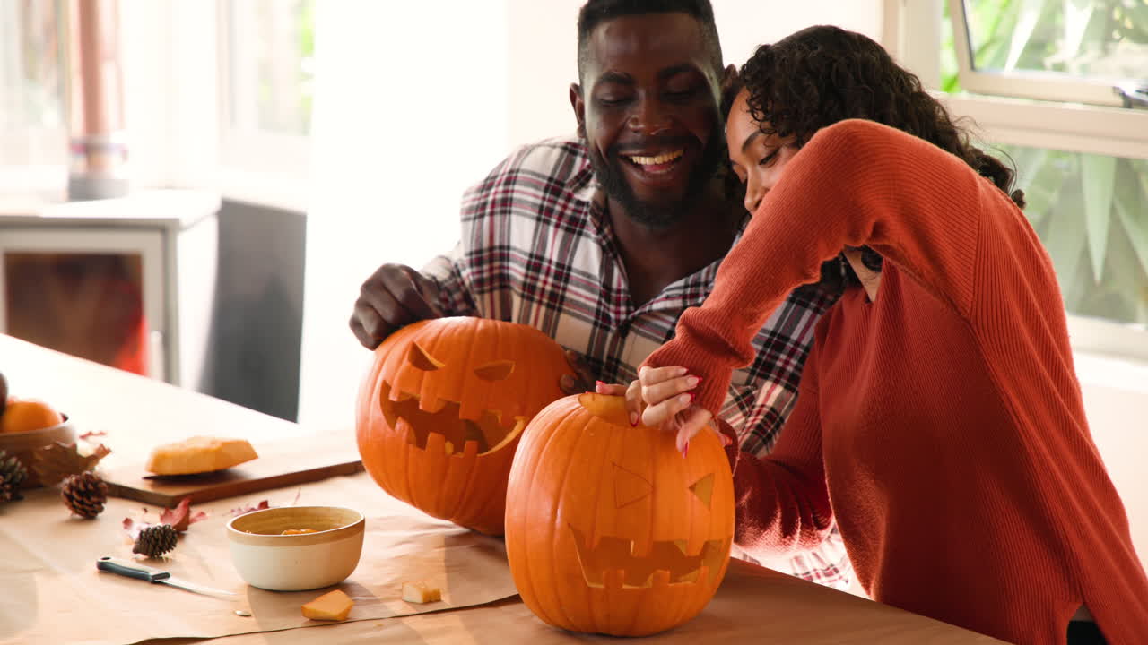 Halloween time, multiracial couple carving pumpkins at home, laughing and enjoying together