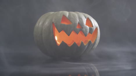 Smoke-effect-over-scary-face-carved-halloween-pumpkin-against-grey-background