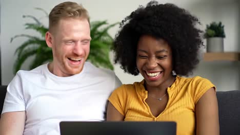 happy interracial couple laughing with laptop at home