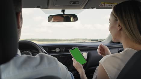 Vista-Trasera-De-Una-Pareja-Caucásica-De-Mediana-Edad-Conduciendo-Un-Automóvil-Y-Usando-Un-Mapa-En-Un-Teléfono-Inteligente.