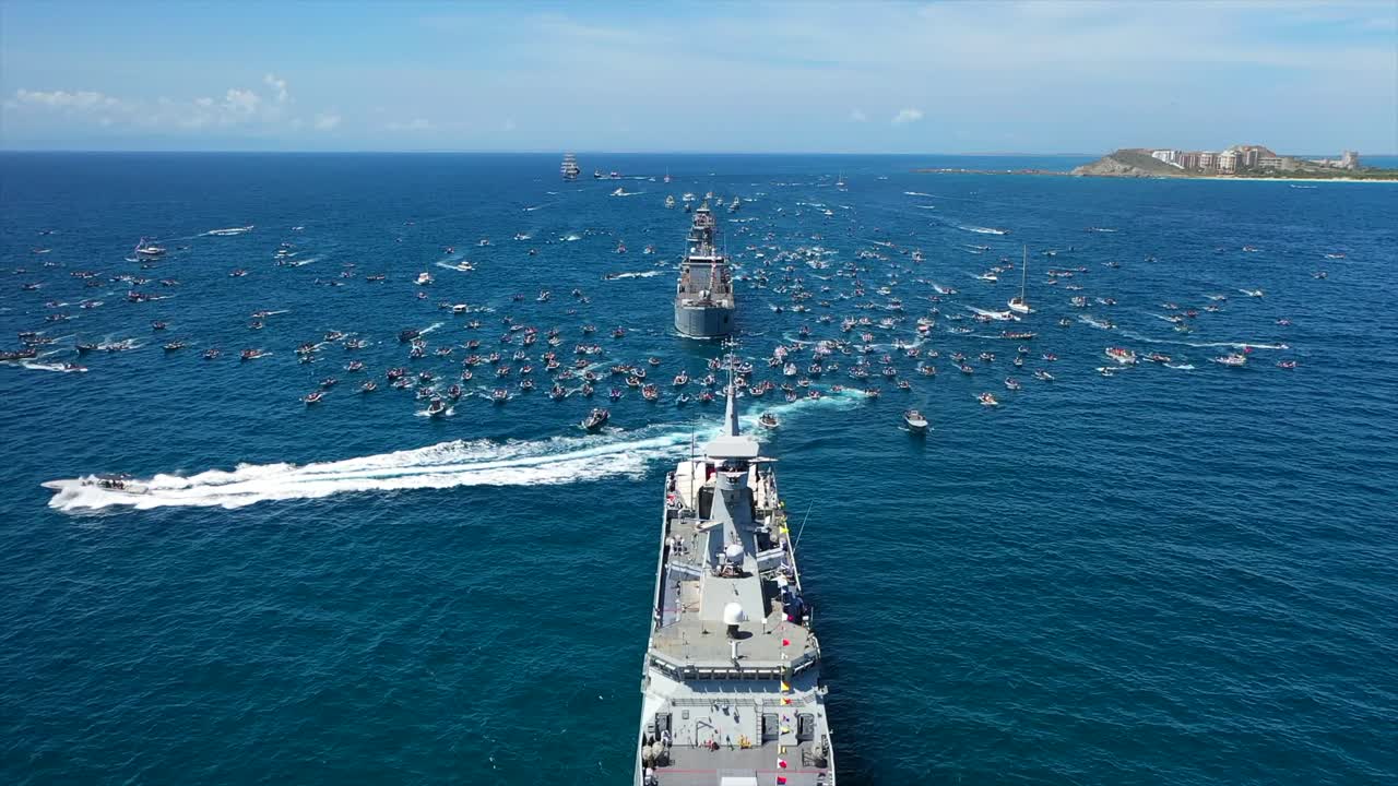 Boats gather near a military ship at sea for a religious procession