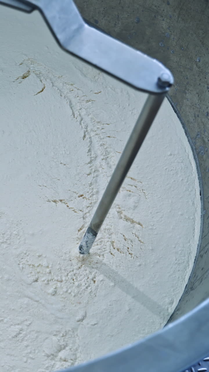 Slow motion of mixer in metal bowl for making cheese. Factory equipment. Metal mixing apparatus boils and mix milk for making cheese at milk products making factory. Vertical video