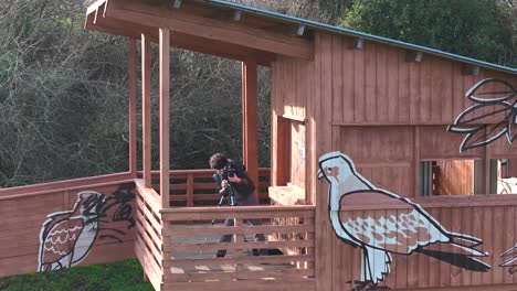 Fotógrafo-De-Viajes-Instalando-Una-Cámara-En-Un-Trípode-En-El-Balcón-De-Una-Cabaña-De-Madera-En-El-Bosque