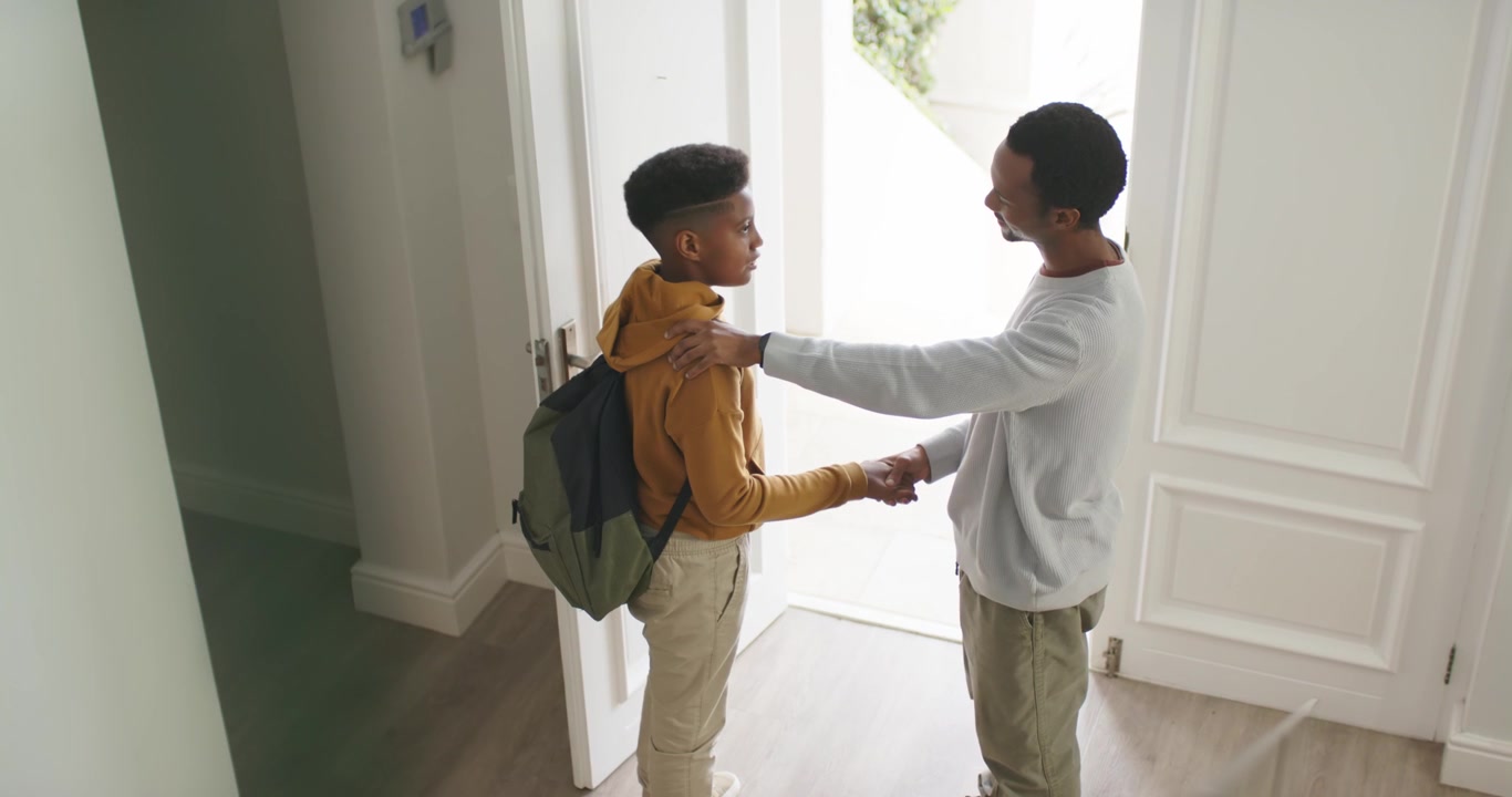 African American dad teen son front door open patting shoulder, handshake son leaving with backpack