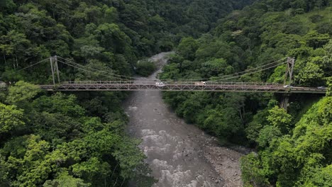 trucks and vans crossing old run down steel bridge in the jungle of south america