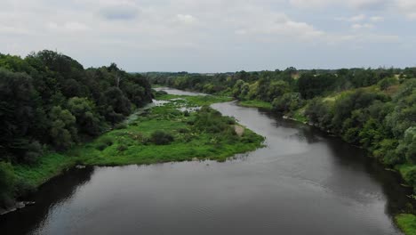 Vista-Aérea-Del-Río-Con-Gruesos-Parches-De-Hierba-En-Un-Día-Nublado-Que-Avanza