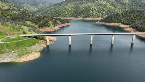 with the lake stretching into the distance, this aerial drone shot captures the don pedro reservoir bridge from above, revealing the seamless connection between nature and human engineering.