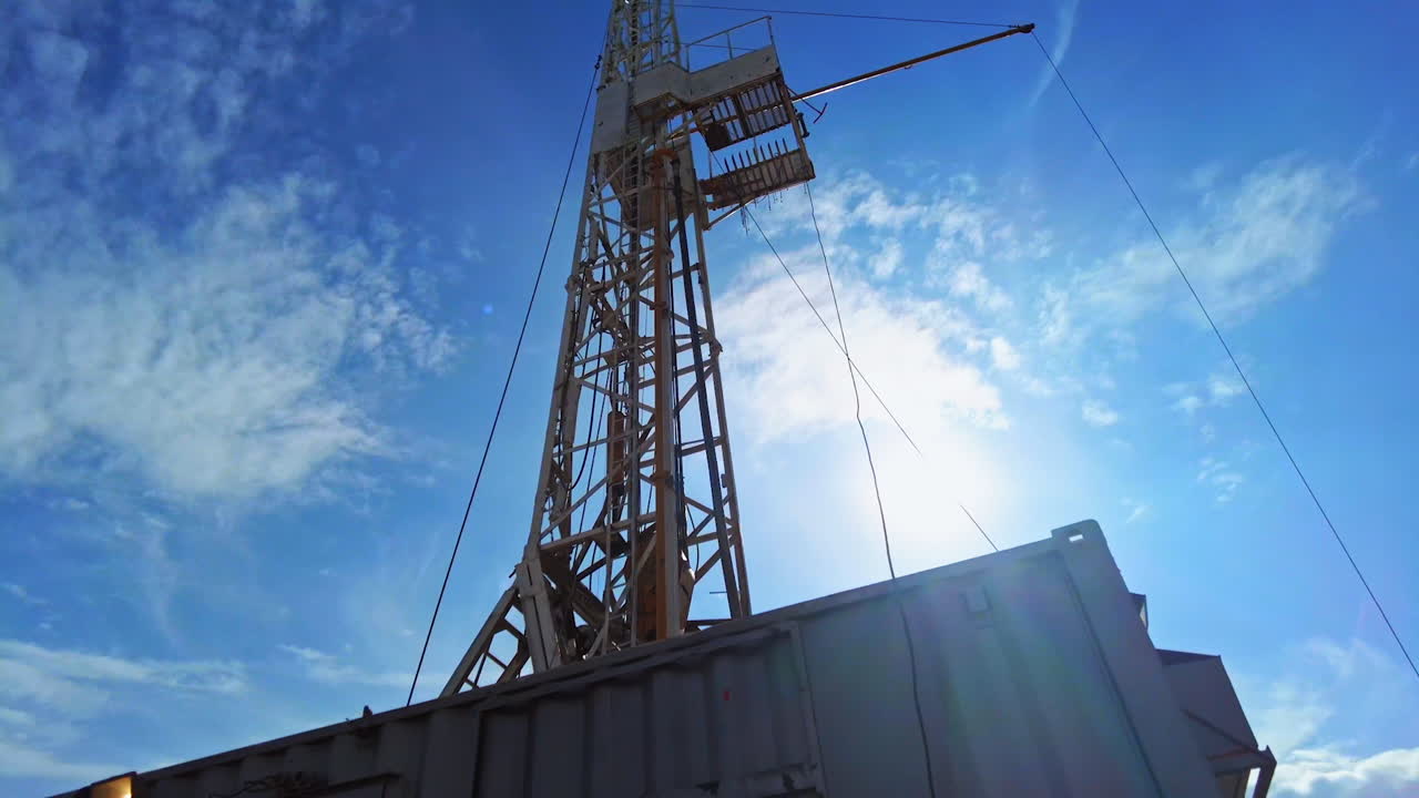 Ser op på det høje boretårn til produktion af olie eller gas. Metaltårn til boring efter ressourcer mod en baggrund af blå himmel